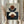 May include: Person in cream ruffle-sleeved top holding framed abstract geometric art print featuring terracotta orange circles and navy blue semicircles on beige background, with dried pampas grass stems, soft natural window lighting in neutral-toned room setting
