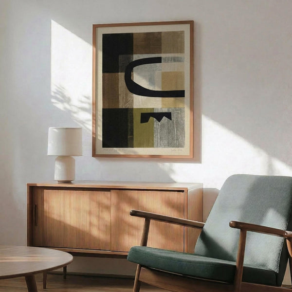 May include: Abstract geometric art print with black curved shapes and rectangular blocks in earth tones of brown, olive, and gray, displayed in thin wood frame above mid-century modern credenza. Sage green upholstered armchair with wooden arms sits nearby, white ceramic table lamp creates warm lighting, sunlight streams across white wall creating dramatic shadows.