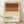 May include: Framed minimalist poster with horizontal color blocks in rust red, warm orange, and cream representing Negroni cocktail ingredients. Bold black text reads "NEGRONI" with ingredients "Gin, Campari, Sweet Vermouth, Orange Twist" below. Light wood frame sits on wooden floor against white textured wall with soft natural lighting and shadows.