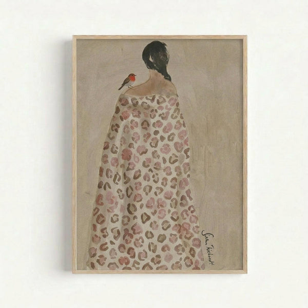 A framed watercolor painting showing a woman from behind wearing a flowing leopard print dress or robe in soft pink and brown tones. She has dark hair in a braid and a small robin with an orange-red breast perches on her shoulder. The artwork has a muted beige background and is displayed in a light wood frame against a white wall. The painting style is soft and dreamy with delicate brushwork.