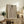 May include: Framed artwork showing a woman with dark hair in a bun wearing a leopard print dress, with a small red bird perched on her shoulder, displayed on a rustic wooden sideboard alongside potted plants, books, and ceramic vases in a warm, neutral-toned living room setting.