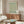 May include: Framed botanical poster with green willow branch pattern on cream background, displayed above mid-century walnut credenza in modern living room with white curved chair, brass floor lamp, oval glass coffee table, and neutral wall color