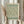 May include: Hands holding a framed botanical art print featuring William Morris's 1887 Willow Bough pattern in sage green tones on cream background. The print shows flowing willow branches and leaves in an intricate repeating design. Light wood frame with white matting against neutral curtained window. Person wearing beige ruffled sleeves holds dried pampas grass stems, creating a soft, natural styling scene.