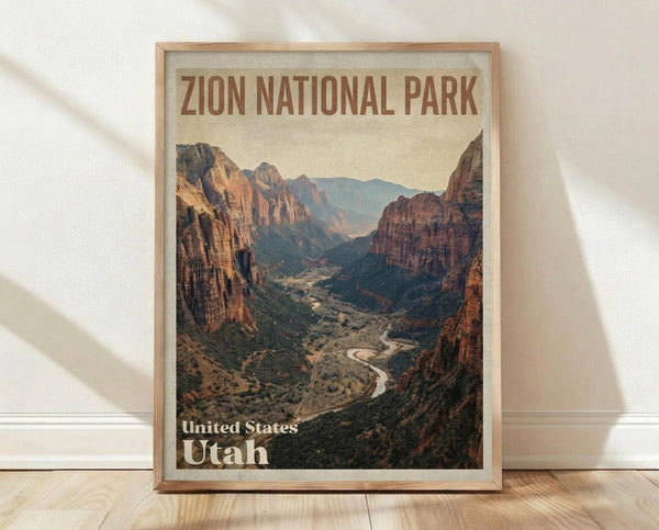 May include: Framed vintage-style travel poster featuring Zion National Park's dramatic red rock canyon landscape with a winding river below. The artwork shows towering sandstone cliffs in warm earth tones against a pale sky, displayed in a natural wood frame leaning against a white wall on light wooden flooring with soft natural lighting.