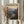 May include: Person holding framed vintage-style travel poster featuring Zion canyon landscape with towering red rock cliffs, winding river, and desert valley. Warm earth tones dominate the design. Light wood frame against neutral curtained background with dried pampas grass visible on left side.
