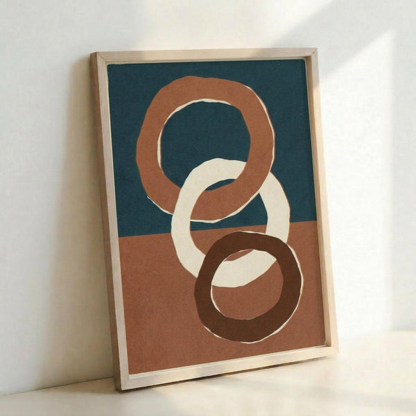 Abstract artwork featuring three interlocking circular rings in terracotta, cream, and dark brown colors against a split background of teal blue and warm brown. The organic, hand-drawn rings overlap and interweave across the composition. Displayed in a light wood frame leaning against a white wall, creating soft shadows.