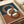Modern abstract art print featuring three interlocking oval rings in terracotta brown, cream, and dark brown against a split background of teal blue and warm terracotta. The geometric design has smooth, flowing curves with subtle dimensional shading. Print is displayed flat on white paper with a light wooden frame border, positioned on a neutral surface next to rolled kraft paper.