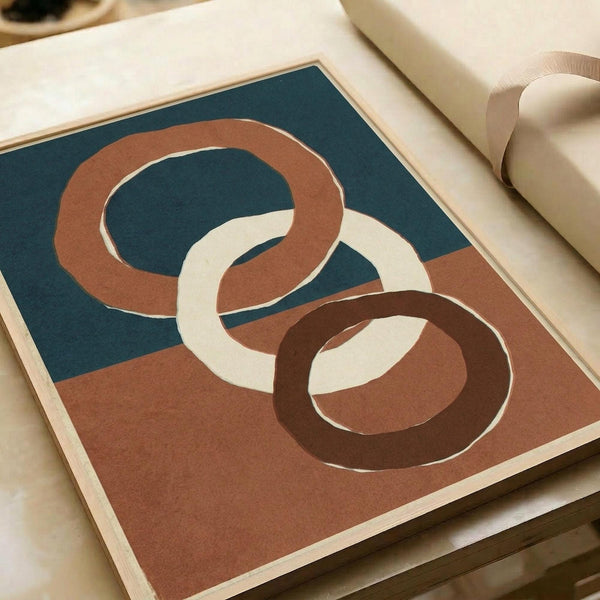 Modern abstract art print featuring three interlocking oval rings in terracotta brown, cream, and dark brown against a split background of teal blue and warm terracotta. The geometric design has smooth, flowing curves with subtle dimensional shading. Print is displayed flat on white paper with a light wooden frame border, positioned on a neutral surface next to rolled kraft paper.
