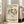 May include: Framed exhibition poster featuring five dancing figures in a circular formation rendered in muted teal, brown, and olive green tones against cream background. Japanese and French text indicates Henri Matisse exhibition at Musée d'Art Moderne de Paris. Light wood frame leans against white wall next to beige upholstered sofa in bright, minimalist living room with large windows and natural light casting shadows.