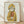 May include: Framed poster print showing a tabby cat wearing a yellow hooded raincoat and holding a red fish, displayed in a light wood frame against a white textured wall on wooden flooring with soft natural lighting creating diagonal shadows