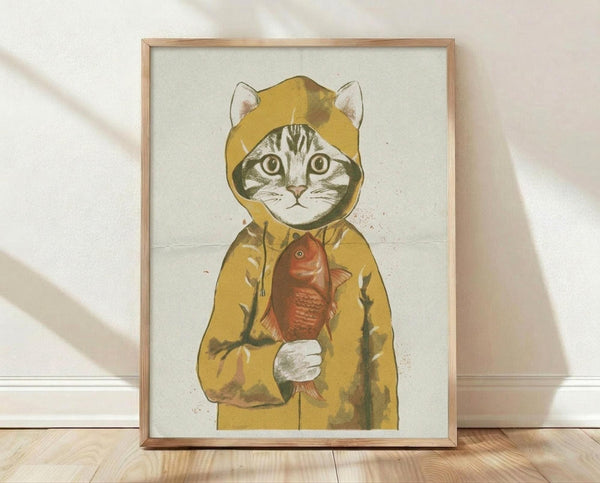 May include: Framed poster print showing a tabby cat wearing a yellow hooded raincoat and holding a red fish, displayed in a light wood frame against a white textured wall on wooden flooring with soft natural lighting creating diagonal shadows