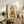 May include: Framed artwork featuring a tabby cat wearing a yellow hooded raincoat and holding an orange fish, displayed on a rustic wooden sideboard alongside books, ceramic vases, a fern plant, and cream-colored furniture in a warmly lit living room setting.