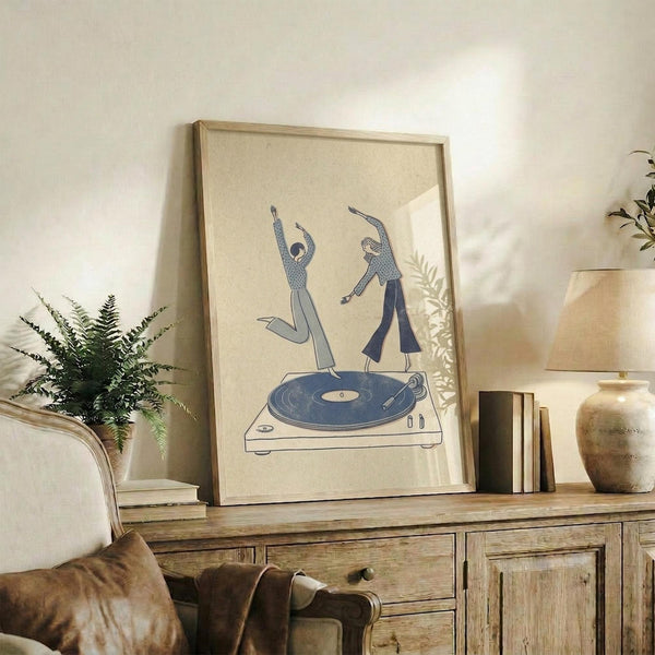 May include: Framed minimalist poster showing two dancing figures in blue tones emerging from a turntable record player, displayed on rustic wooden sideboard alongside fern plant, ceramic vase, and stacked books in warm neutral living room setting with cream armchair visible