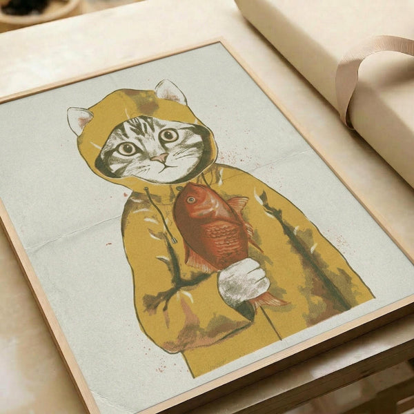 Framed print showing a tabby cat wearing a yellow hooded raincoat and holding a red fish. The artwork has a vintage illustration style with muted colors on light background. The wooden frame sits on a white surface next to cream-colored ribbon, creating a soft, neutral setting.