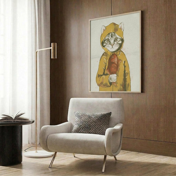 May include: Framed poster artwork displayed on wood-paneled wall above beige upholstered armchair with geometric pillow. Art shows tabby cat wearing yellow hooded raincoat holding orange fish, rendered in whimsical illustration style with muted colors. Modern living room setting with brass floor lamp, round side table with open book, and natural lighting from window with curtains.