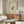 May include: Framed vintage Japanese frog artwork hanging above a mid-century walnut credenza in a minimalist living room. The cream-colored print features a detailed black ink frog illustration with Japanese characters. Modern white curved chair and glass-top coffee table with abstract blue and yellow art visible. Warm wood tones complement the neutral beige walls and natural lighting.