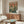 May include: Framed anime-style poster showing mecha robot and pilot character against futuristic cityscape in rain, displayed above walnut credenza in modern living room with white sculptural chair, glass coffee table, and table lamp