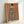 May include: Framed art print leaning against white wall showing woman from behind wearing zebra-striped cloak or dress, with dark braided hair and small blue bird perched on shoulder, painted on warm peachy-orange background, displayed in light wood frame on white surface