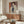 May include: Modern living room interior with abstract portrait artwork on wall above wooden sideboard. Painting features stylized figure with geometric face in warm tones of orange, purple, and navy blue. Room has cream walls, white upholstered chair, glass coffee table, and contemporary lighting fixtures creating bright, minimalist space.