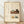 May include: Framed poster with cream background featuring Japanese calligraphy text and watercolor illustrations of kitchen items including a wooden table with dark mug, small potted plant, pastries on a plate, and green teacup. Light wood frame rests against white wall on wooden floor with soft natural lighting creating diagonal shadows.