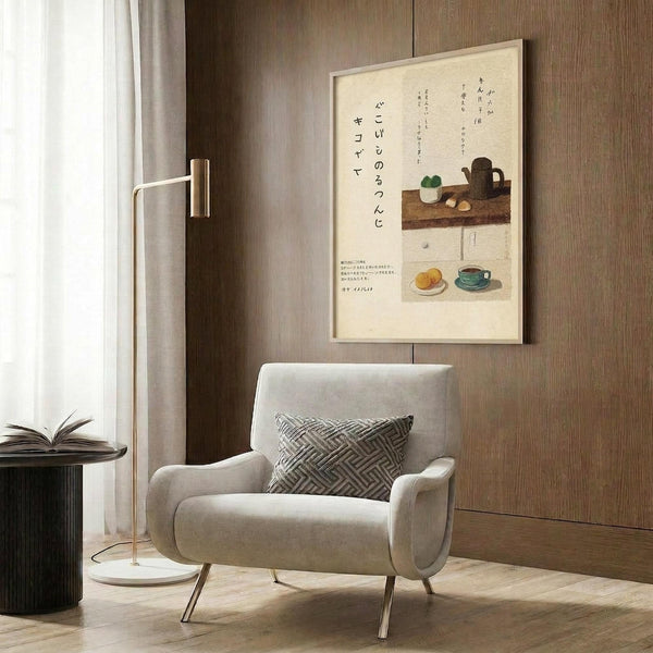 May include: Framed Japanese calligraphy poster with kitchen still life illustrations hanging on wood-paneled wall above beige armchair. Artwork features black vertical text, teapot, bowls, and coffee cup in muted earth tones on cream background. Modern reading nook with geometric pillow, brass floor lamp, and dark round side table with open book.