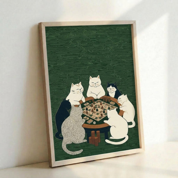 May include: Framed poster print leaning against white wall showing five cats gathered around wooden table playing board game on green textured background. Cats include white, black and white, striped gray, and cream colored felines sitting contentedly around chess or checkers board. Light wooden frame, approximately 12x16 inches, displayed on white surface with soft natural lighting creating gentle shadows.