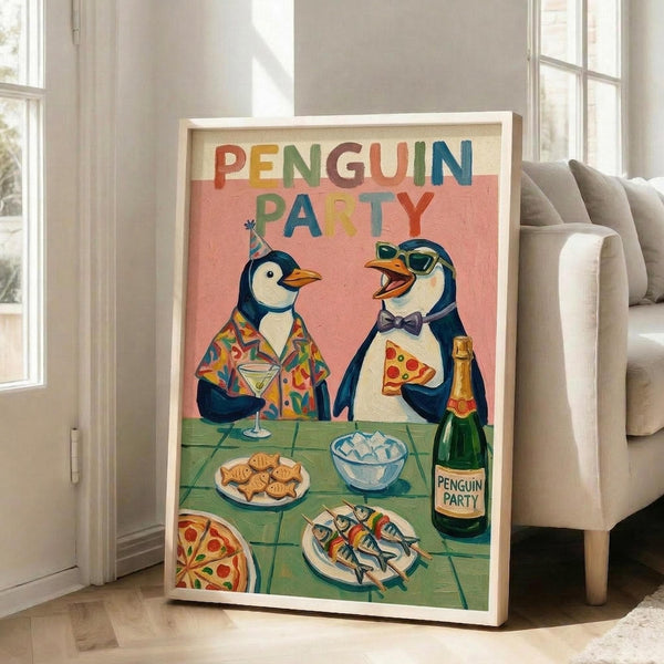 May include: A framed poster leaning against a white wall next to a beige couch in a bright living room. The colorful artwork shows two penguins at a party - one wearing a tropical shirt holding a martini, another in sunglasses and bow tie with pizza slice and champagne bottle. The scene includes a table with fish, cookies, and ice bucket on turquoise tiles. Text reads "PENGUIN PARTY" in rainbow letters against a coral pink background.