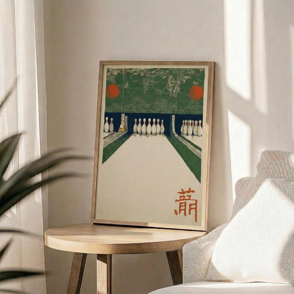May include: Vintage Japanese woodblock print artwork displayed in light wood frame on round wooden side table next to beige upholstered chair. Print depicts bowling alley with green walls, white pins, orange circular lights, and red Japanese characters in corner. Sunlight streams across white wall creating shadows, with plant leaves visible at left edge.