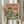 May include: Hands holding a framed poster featuring two cats wearing sunglasses at a party table with colorful text reading "CAT PARTY" at top. The tabby cats hold cocktail glasses with party foods like tuna, cheese, and toy mice scattered on green surface. Bottle labeled "CATNIP FIZZ" sits nearby. Pink background, light wood frame, person in cream sweater holds dried wheat stems in soft natural lighting by white curtains.