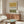 May include: Abstract art print with ochre yellow and olive green watercolor blocks separated by black and white tribal geometric patterns, displayed in thin wooden frame above mid-century walnut credenza. Modern living room setting with cream curved chair, oval glass coffee table, and contemporary table lamps on neutral walls.