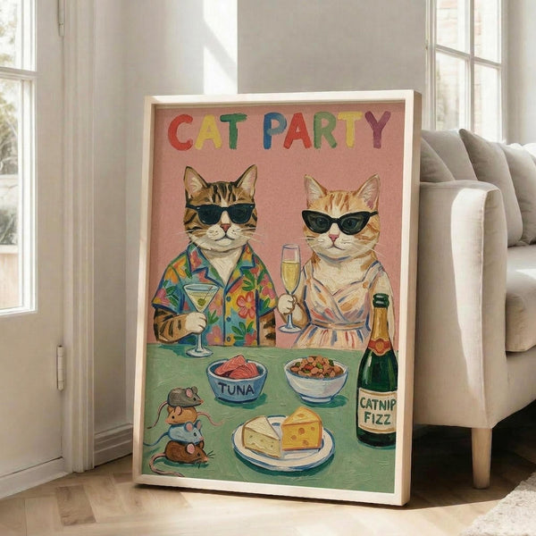 May include: Framed poster with pink background showing two cats wearing sunglasses at a party table. Left cat wears colorful Hawaiian shirt holding martini, right cat in light dress holds champagne flute. Green table displays tuna bowl, kibble bowl, cheese wedges, catnip fizz bottle, and toy mice. Colorful "CAT PARTY" text at top. Light wood frame leans against white wall next to beige couch in bright room with windows.