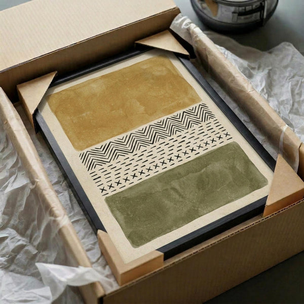 May include: Framed abstract art print with horizontal bands in ochre yellow and olive green separated by geometric tribal patterns in black and white. Print displayed in light wood frame, surrounded by brown cardboard packaging materials and wrapped wooden dowels on white tissue paper.