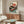 May include: Japanese-style vintage poster featuring red turntable with black vinyl record, orange sun, cherry blossoms, and bonsai trees, displayed above mid-century walnut credenza in modern living room with white curved chair, brass floor lamp, and glass coffee table on cream walls