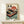 May include: Framed vintage-style poster featuring a red turntable with cherry blossoms and Japanese text against a sunset backdrop with bonsai trees, displayed on a light wood shelf next to a small white wrapped gift with natural twine and dried sprig accent.