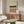 May include: Abstract geometric poster with horizontal bands in sage green, coral pink, white with black dots, displayed in wooden frame above mid-century walnut credenza. Modern living room setting with cream sculptural chair, oval glass coffee table, and minimalist decor on neutral walls.