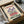 May include: Vintage-style poster print with cream background featuring purple iris flowers and red blooms, text reading "Flower Market" and "Amsterdam" in red and green lettering. Black wooden frame shown in cardboard shipping box with brown paper wrapping and tissue paper on white surface.