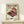 May include: Vintage-style Japanese poster featuring a red turntable with vinyl record, cherry blossom branches, stylized sun, and bonsai tree. Black Japanese text on cream background. Displayed in light wood frame on white shelf next to small wrapped gift with twine and greenery sprig against white wall.