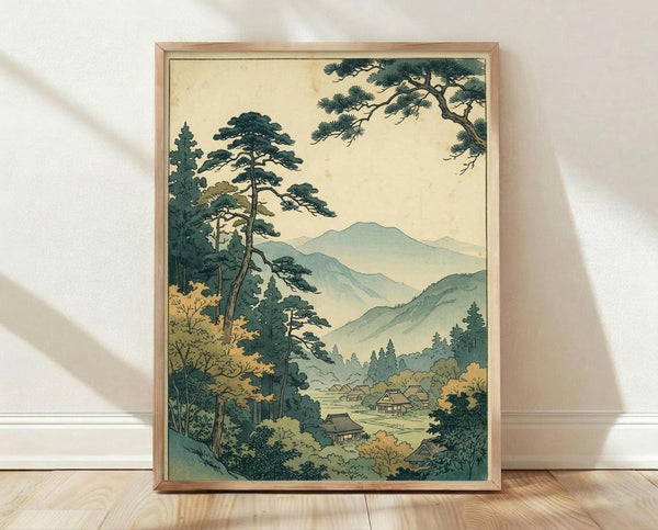May include: Framed vintage Japanese woodblock print showing mountain landscape with pine trees, traditional houses nestled in valley, layered blue-green mountains in background. Warm cream sky contrasts with teal and sage green foliage. Natural wood frame sits on light wooden floor against white wall with soft shadows.