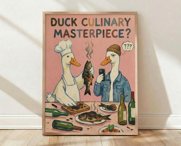 May include: Framed poster print leaning against white wall on light wood floor. Pink background artwork shows two anthropomorphic ducks - one wearing chef's hat and apron, another in beanie and denim jacket holding phone with question marks above head. Chef duck holds cooked fish while kitchen counter displays prepared fish dishes, wine bottles, and cooking ingredients. Humorous illustrated style in muted pastels with natural wood frame.