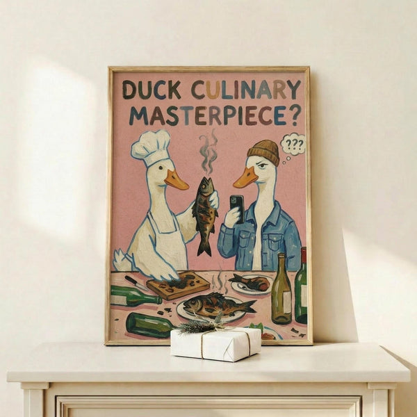 May include: Framed poster print with pink background showing two white ducks - one wearing chef's hat and apron cooking fish, another in beanie and denim jacket holding phone with confused expression. Kitchen scene includes cutting board, cooked fish, wine bottles, and vegetables scattered around. Natural wood frame displayed on light wooden shelf next to small white wrapped gift with twine and herb sprig.