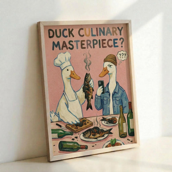 May include: Framed poster print leaning against white wall corner showing two anthropomorphic ducks in pink-toned illustration. Left duck wears white chef's hat and apron, holding cooked fish. Right duck in beanie and denim jacket holds phone with confused expression. Scene includes wine bottles, plates of fish, cutting board, and kitchen items scattered on counter surface.