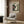 May include: Vintage-style poster featuring turntable with vinyl record and Japanese text, displayed in modern living room with beige upholstered chair, geometric throw pillow, brass floor lamp, and wood-paneled wall. Poster shows retro hi-fi equipment advertisement design in cream and dark colors within light wooden frame.