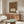 May include: Ornate Victorian-style poster with intricate floral border in rich reds, greens, and golds featuring a decorative bird among flowering vines. Text reads "ART & SOCIALISM" in Gothic lettering. Displayed above a mid-century modern walnut credenza in a minimalist room with white walls, alongside a curved white chair, brass floor lamp, and oval glass coffee table.