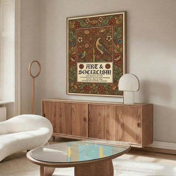 May include: Ornate Victorian-style poster with intricate floral border in rich reds, greens, and golds featuring a decorative bird among flowering vines. Text reads "ART & SOCIALISM" in Gothic lettering. Displayed above a mid-century modern walnut credenza in a minimalist room with white walls, alongside a curved white chair, brass floor lamp, and oval glass coffee table.