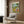May include: Framed poster showing two cartoon ducks doing yoga poses outdoors, with wine glasses and French bread nearby. The colorful illustrated print hangs on wood-paneled wall above a cream-colored modern armchair with geometric pillow. Room features gold floor lamp and dark side table with open book.