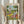 May include: Person in cream ruffled sleeves holding framed poster print near window with dried wheat stems. Artwork shows two cartoon ducks doing yoga poses outdoors - one in floral yoga outfit holding wine glass overhead, another in striped shirt on pink mat. Scene includes yoga blocks, wine bottle, baguettes, and picnic items scattered on grass under trees. Colorful illustrated style with soft lighting.