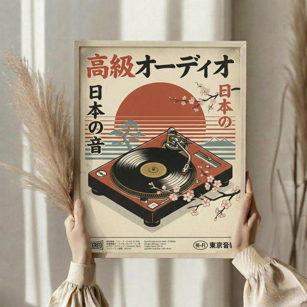 May include: Person in cream ruffle-sleeve top holding framed vintage-style poster featuring red turntable with cherry blossoms against sunset backdrop with Mount Fuji silhouette. Japanese text in red and black characters across top. Dried pampas grass visible on left side. Neutral home interior with white curtains in background.