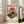 May include: Framed vintage-style Japanese poster featuring orange turntable with vinyl record against cream background, red sun with cherry blossoms, Japanese text in red and black characters, displayed on light wooden floor next to beige upholstered chair in bright room with white walls and large windows