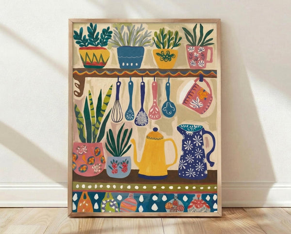 May include: Framed colorful folk art style kitchen illustration showing three shelves with potted plants, hanging utensils, teapots, mugs, and decorative bowls. Features bright blues, yellows, pinks, and greens with floral and geometric patterns. Natural wood frame sits on light wooden floor against white wall with soft shadows.