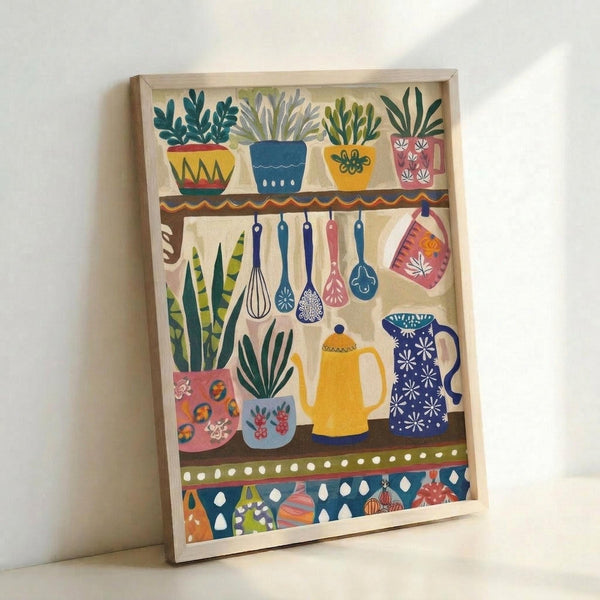 May include: Framed kitchen-themed folk art print leaning against white wall. Colorful illustration shows wooden shelves with potted plants, hanging utensils including whisk and ladles, teapots in yellow and blue with decorative patterns, and ornamental border. Artwork features warm earth tones, botanical elements, and traditional folk art styling in light wood frame.
